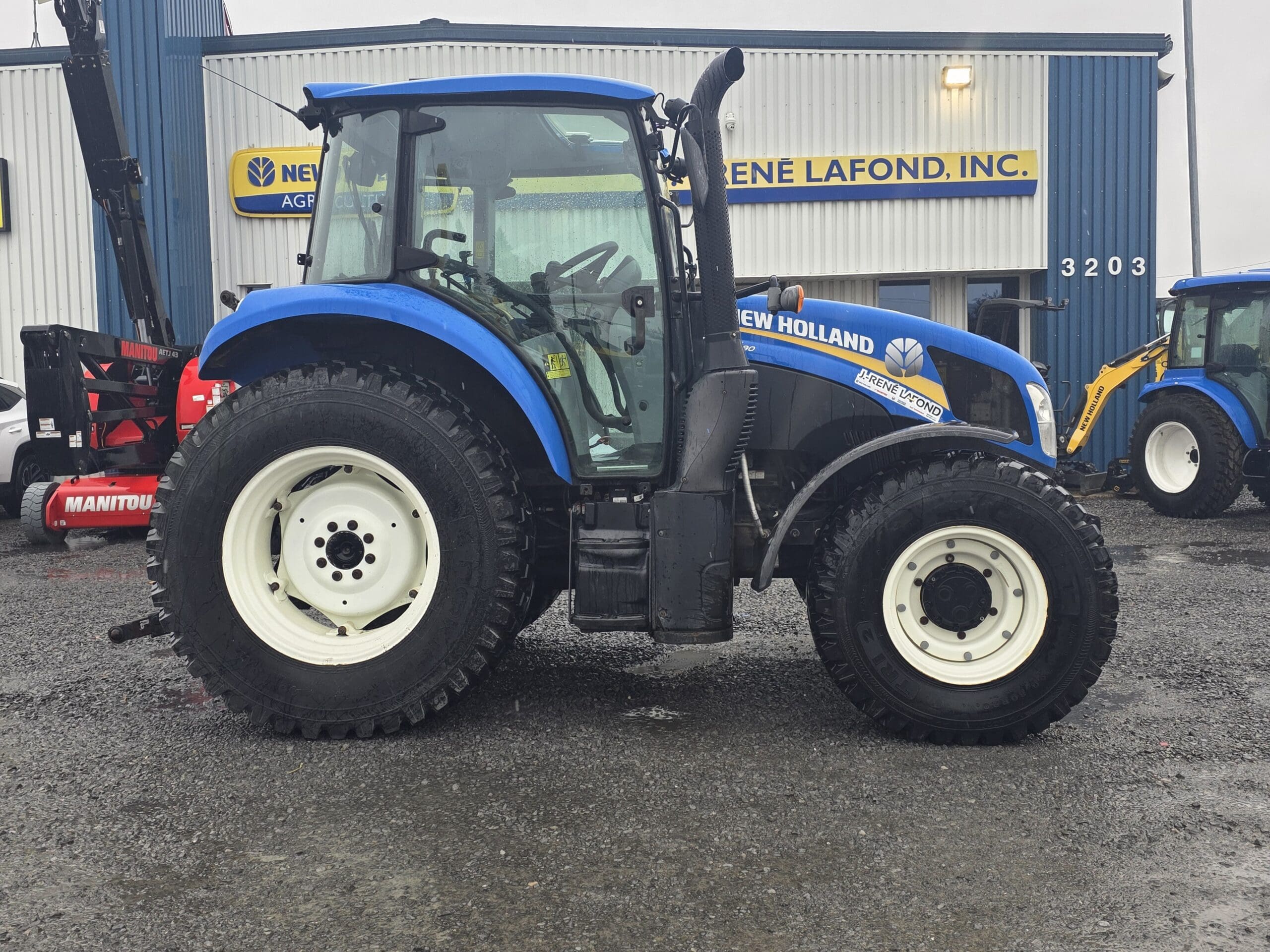 Un tracteur New Holland bleu garé sur le parking d'un concessionnaire, devant un bâtiment portant l'enseigne « René Lafond, Inc. ».