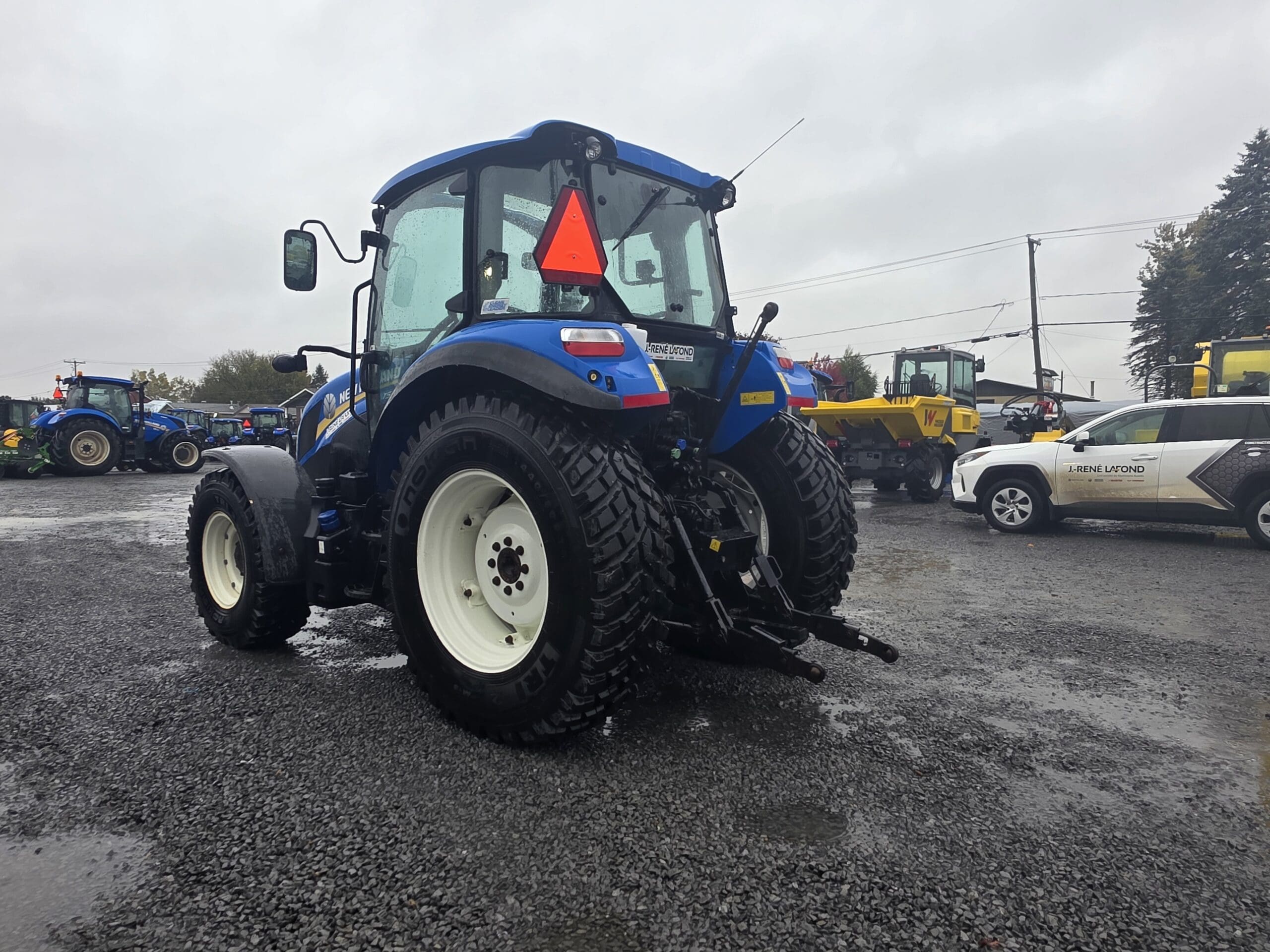 Un tracteur New Holland bleu garé sur un parking extérieur en gravier.