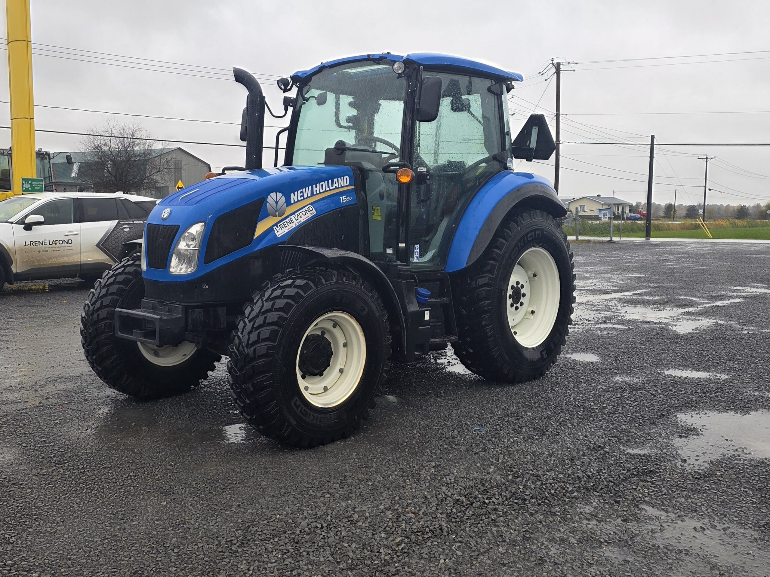 Tracteur New Holland T5.90 bleu garé sur un terrain en gravier.