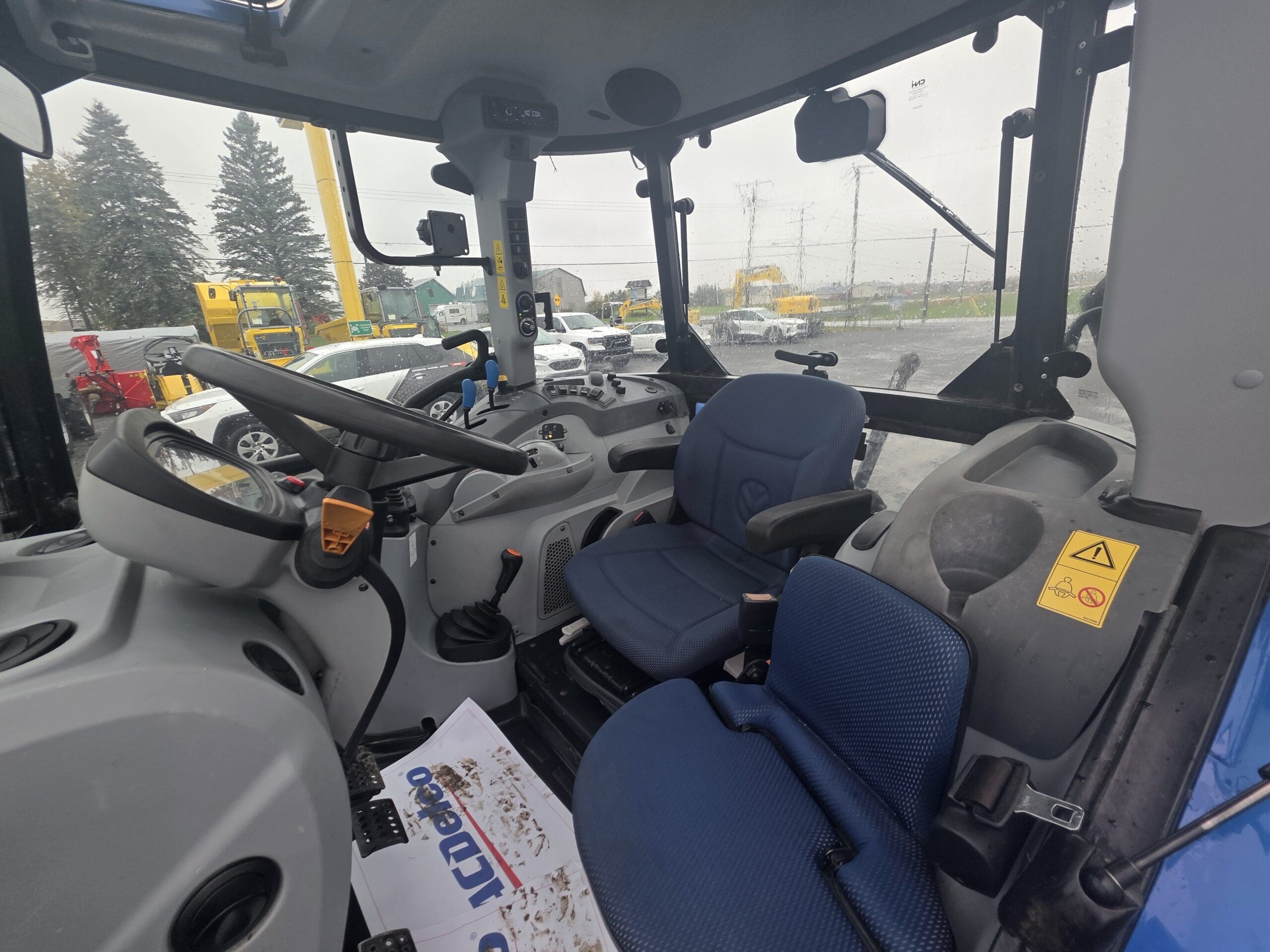 Vue intérieure depuis le siège conducteur d'un tracteur, montrant le volant, les commandes et les sièges bleus.
