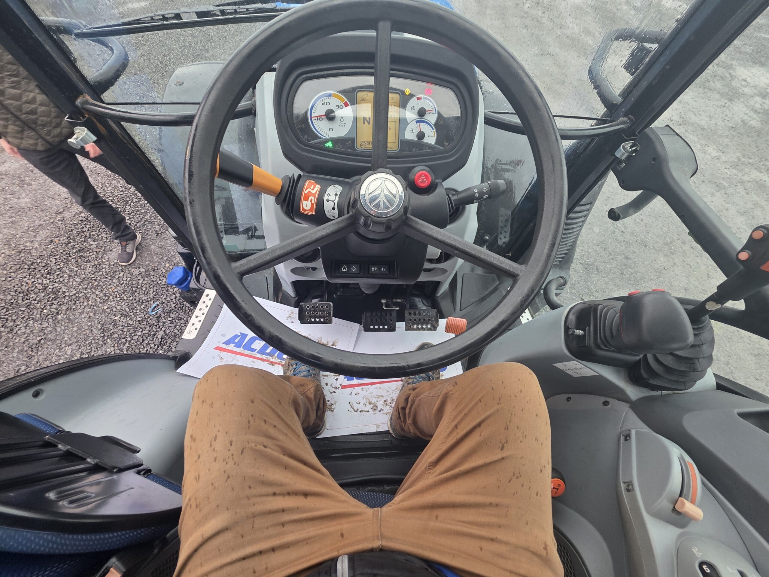 Vue depuis le siège conducteur d'un tracteur, montrant le volant, les jauges du tableau de bord et les pédales.