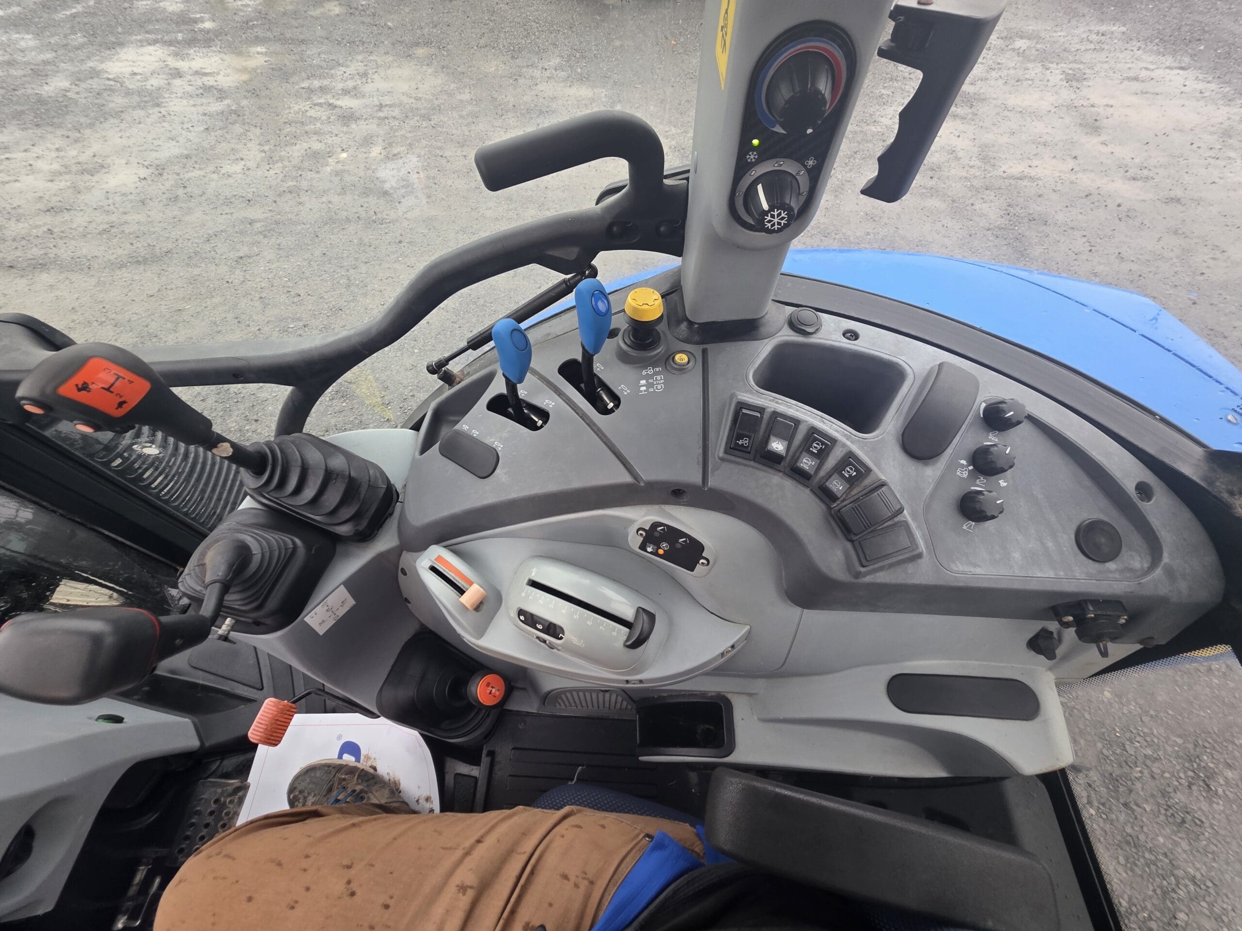 Vue depuis l'intérieur de la cabine d'un tracteur, donnant sur le tableau de bord équipé de divers leviers, boutons et interrupteurs.