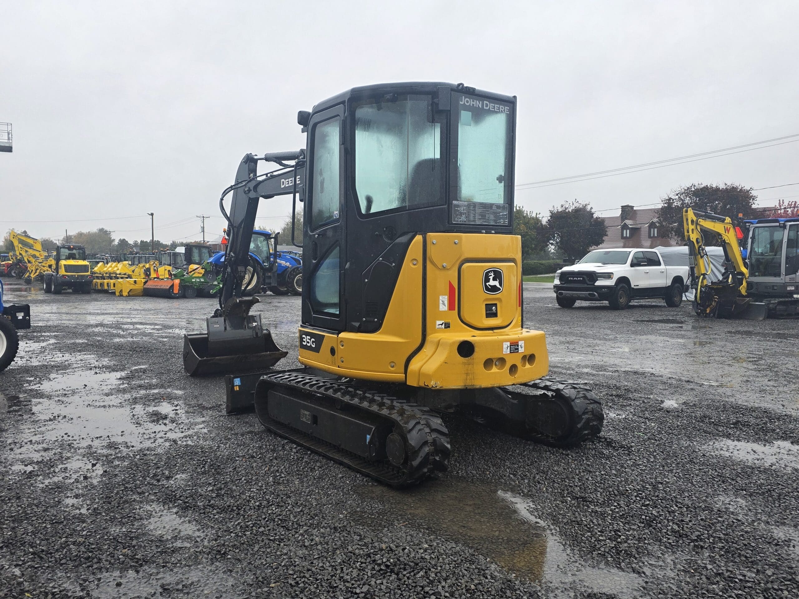 Une pelle compacte John Deere 35G jaune garée sur un terrain en gravier détrempé.