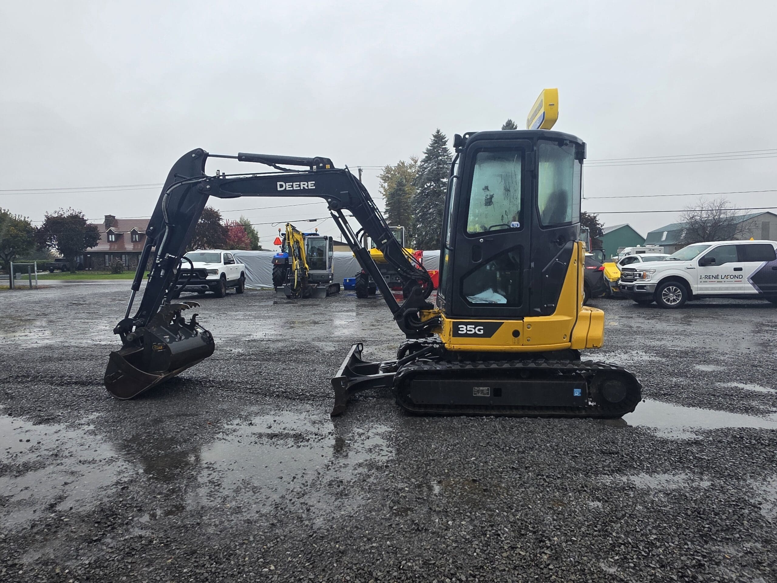 Une pelle compacte John Deere 35G jaune et noire, garée sur un terrain en gravier.