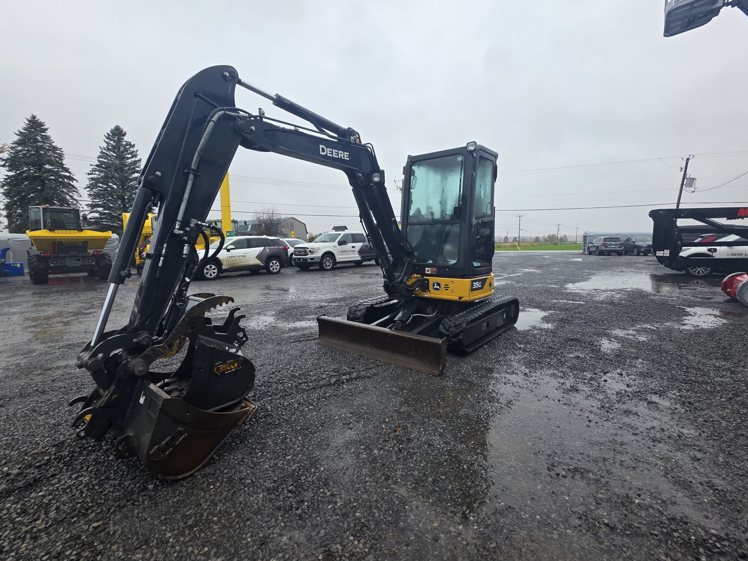 Une pelle compacte John Deere 35G jaune et noire garée sur un terrain en gravier.