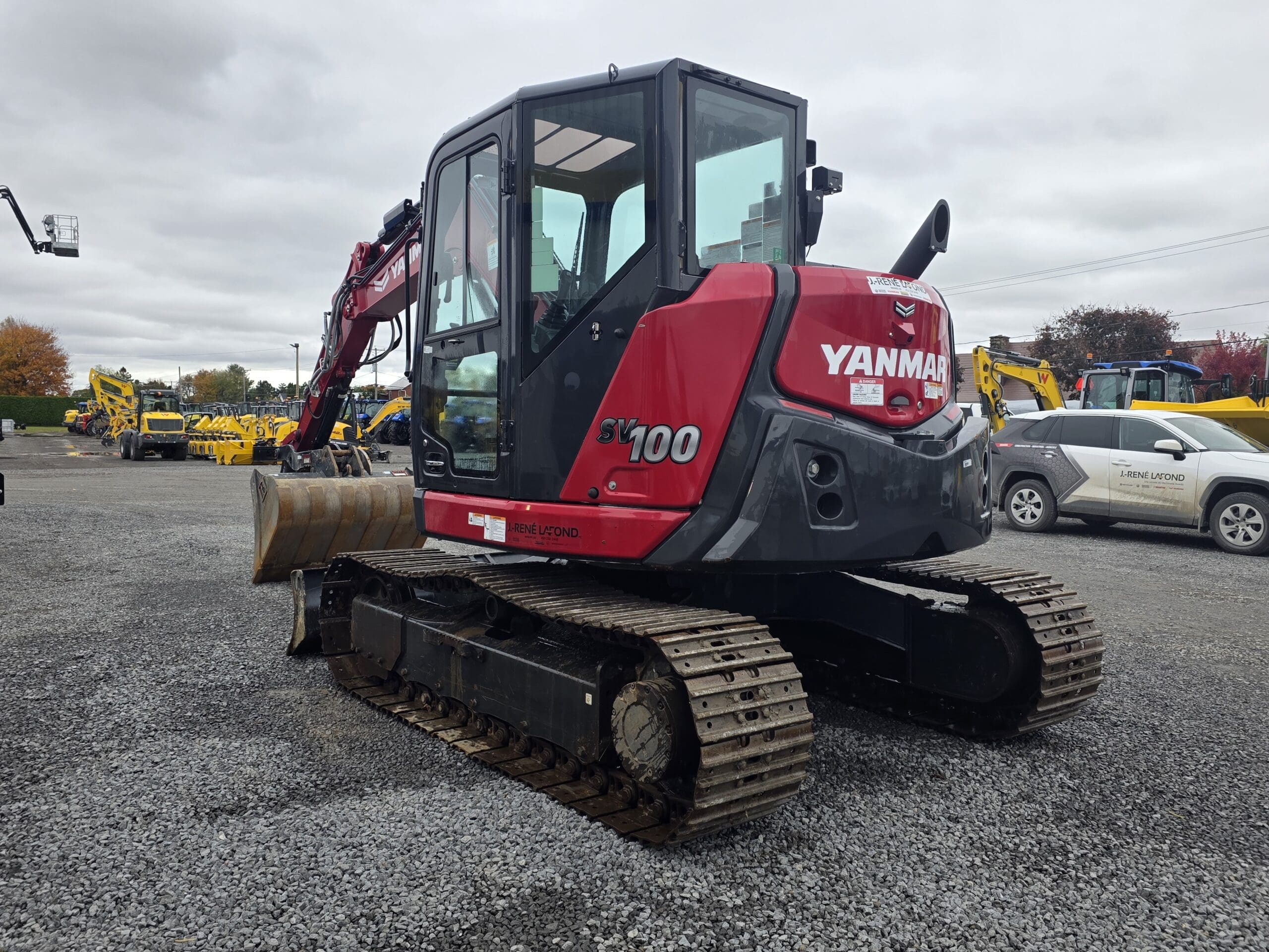 Une pelleteuse sur chenilles Yanmar SV100 rouge garée sur un terrain en gravier.