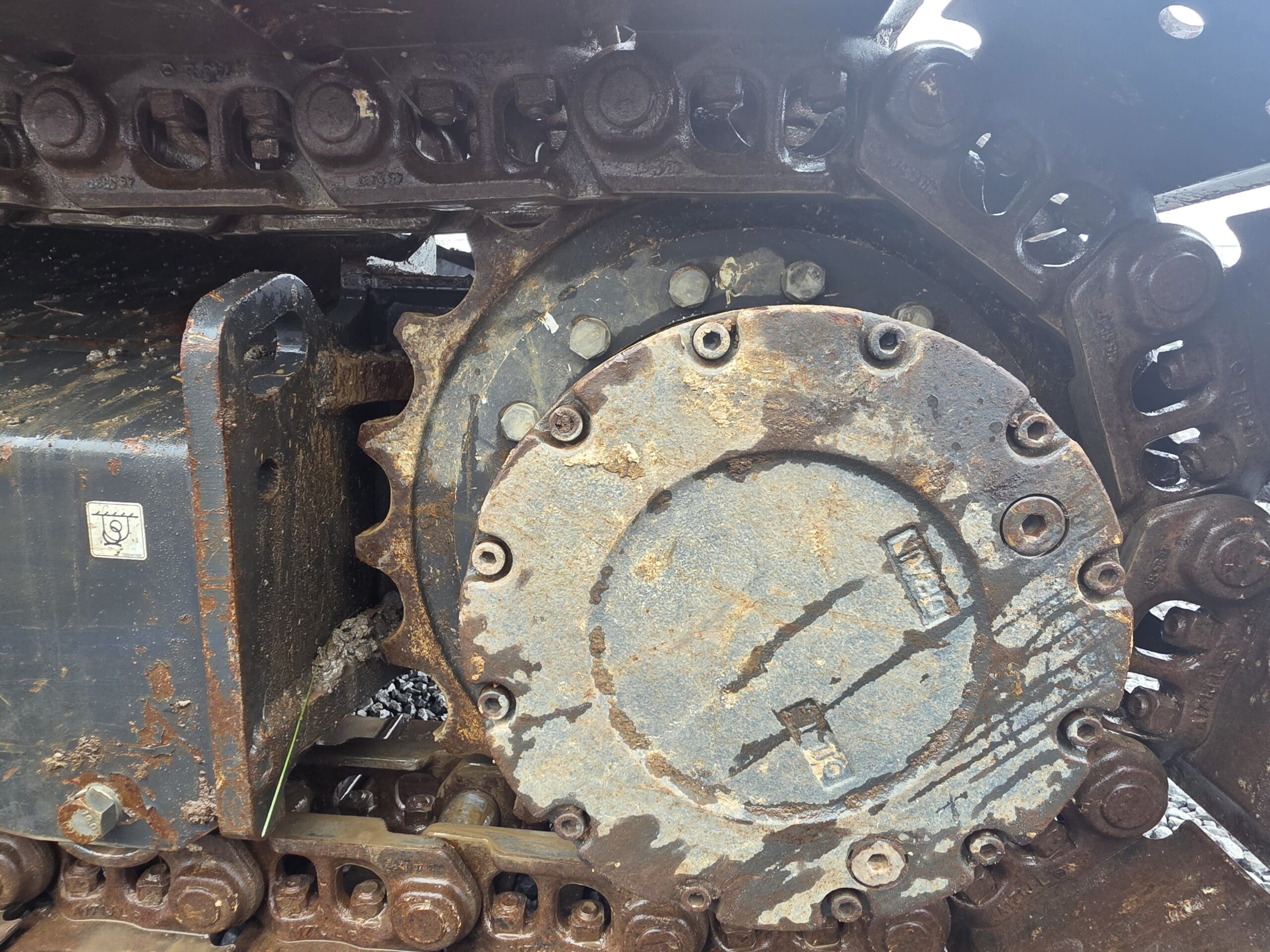 Gros plan sur un pignon métallique boueux et des maillons de chenille ultra-résistants sur un engin de chantier.